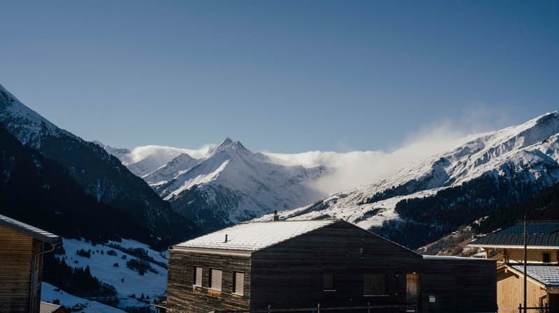 wooden house, snow on the roof, mountains in the background