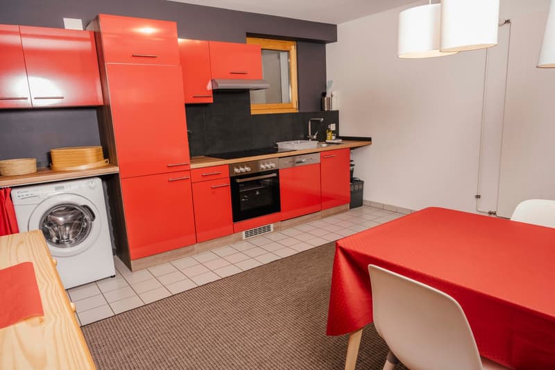 modern kitchen with red cabinets, white appliances, tiled floor, and a dining area with a red tablecloth