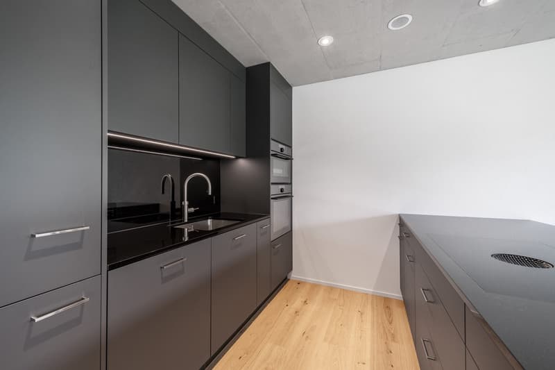 modern kitchen with grey cabinets, wooden floors, black countertops, integrated oven and dishwasher, stainless steel faucet