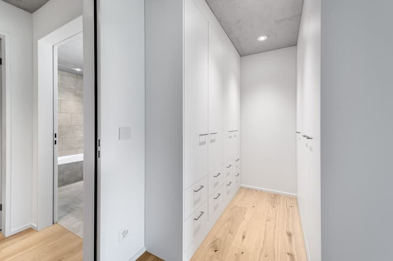 wooden floor, multiple white drawers, tiled bathroom visible through open door