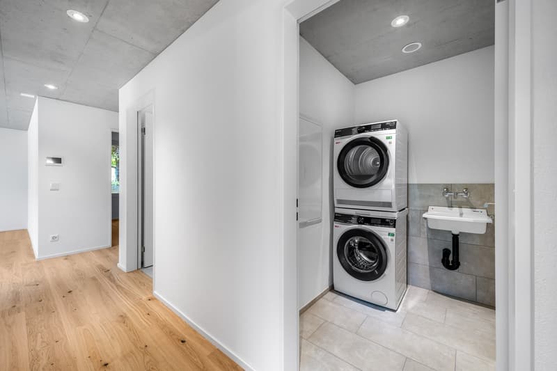 Modern laundry room with white walls and hardwood floor, stackable washer and dryer, sink, power outlet