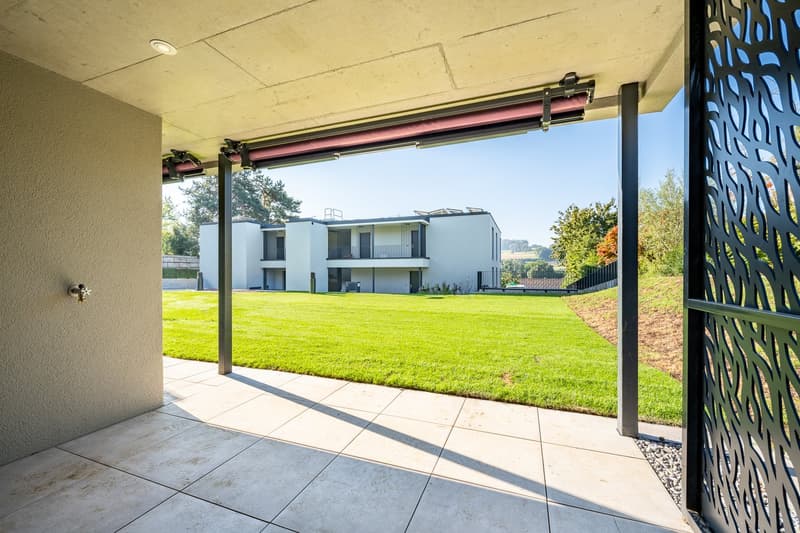 an open patio with tile floor, metal railings, a building behind, and a lawn in the background.