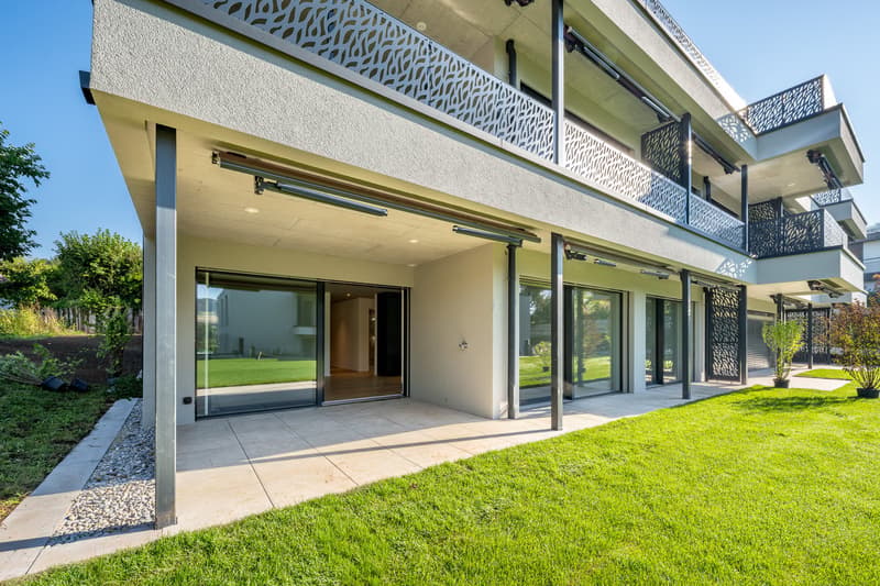 Modern, multi-story building, large glass windows, covered outdoor area, balcony, green landscape