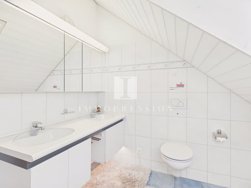 Bathroom with two sinks, toilet, and a mirror, white tiles, and a rug