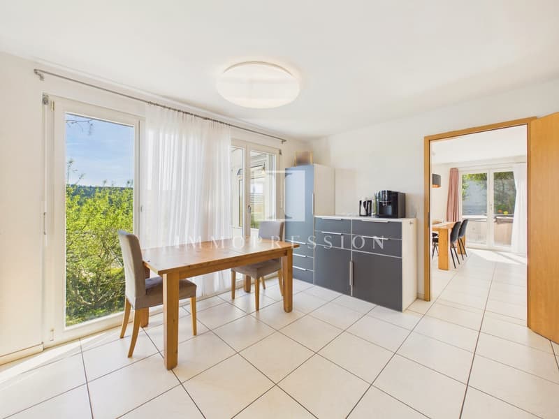 Dining room with a wooden table, chairs, and a glass door leading to a balcony with a view of trees and mountains.