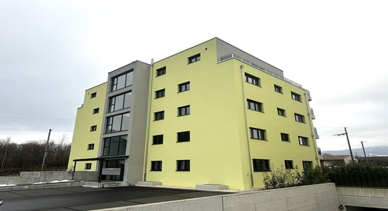 Yellow apartment building, 6 floors, multiple windows, ground floor balcony, concrete fence