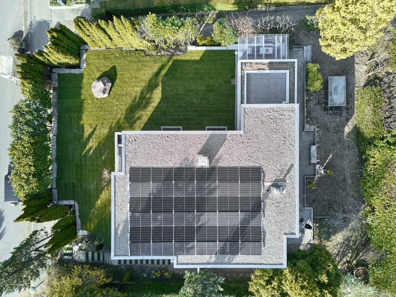 Modern house with solar panels on the roof, surrounded by a well-maintained lawn and trees.
