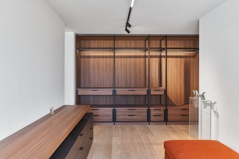 walk-in closet with wooden shelves, drawers, and a hanging rail, wooden desk, white walls, wooden floor, and a glass display case
