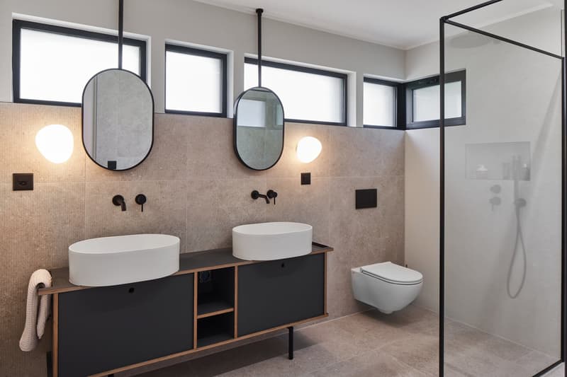modern bathroom with two sinks, a toilet, a shower, and a glass shower door