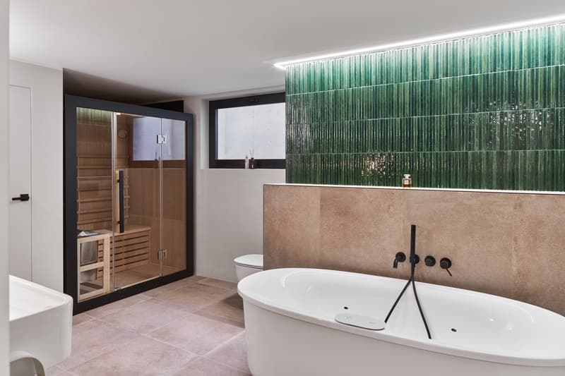 white bathtub, green tiled wall, wooden sauna, white toilet, white sink