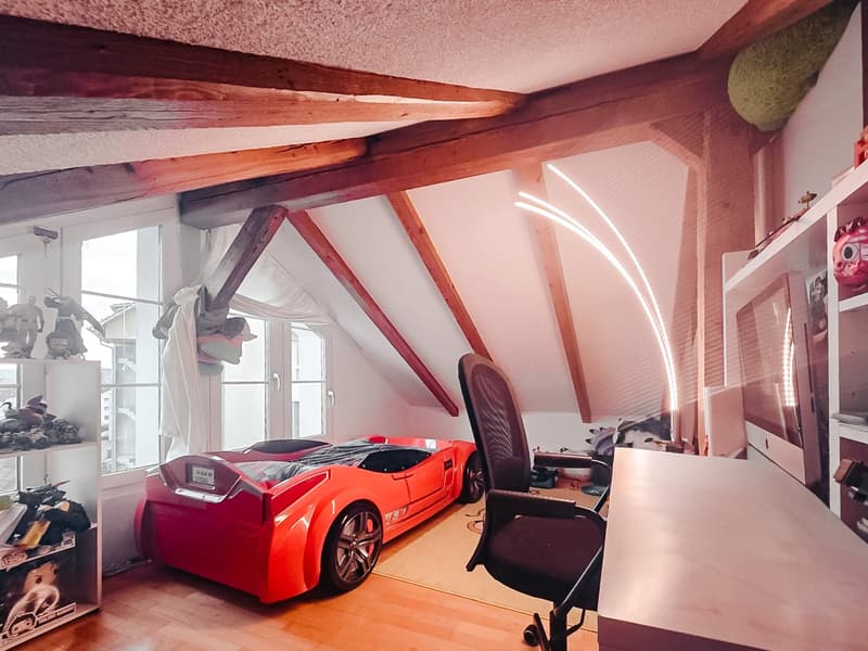 attic room with wooden beams, red sports car bed, desk, chair, shelves with toys, windows