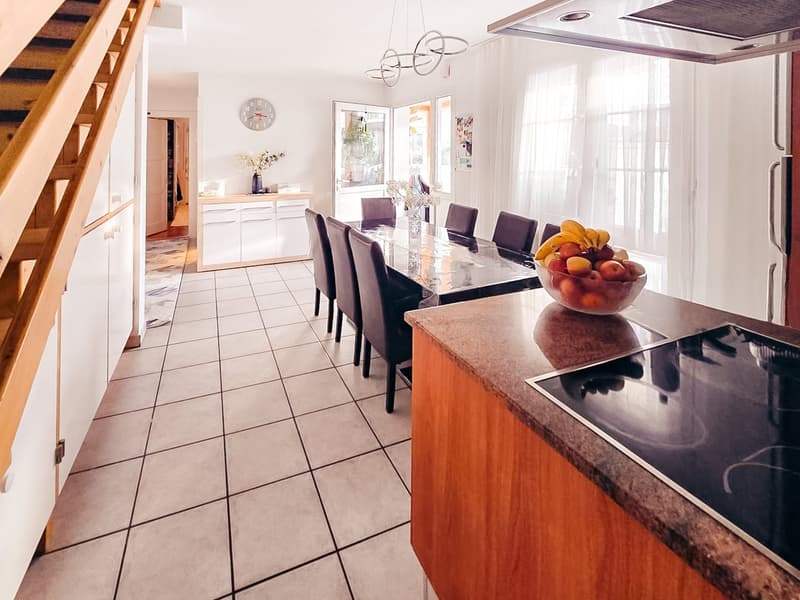 Dining room with a large table, chairs, and a bowl of fruit on the counter