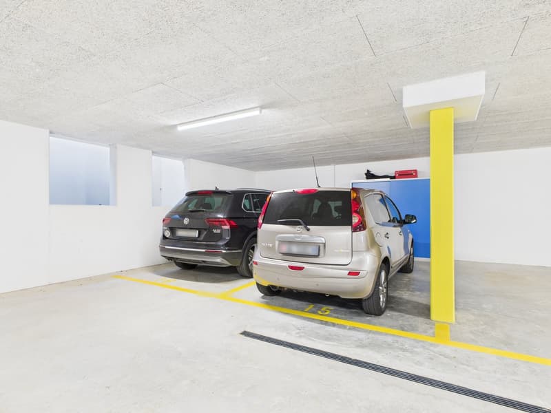 underground parking lot with 2 cars parked and white walls