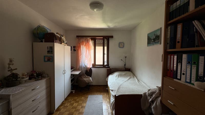 The image shows a bedroom with a bed, dresser, bookshelf, and window. The room has a cozy and lived-in feel, with personal items and decor visible.