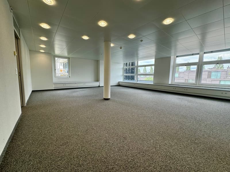 empty room, beige carpeted floor, white walls, three large windows, ceiling-mounted lights, central pillar