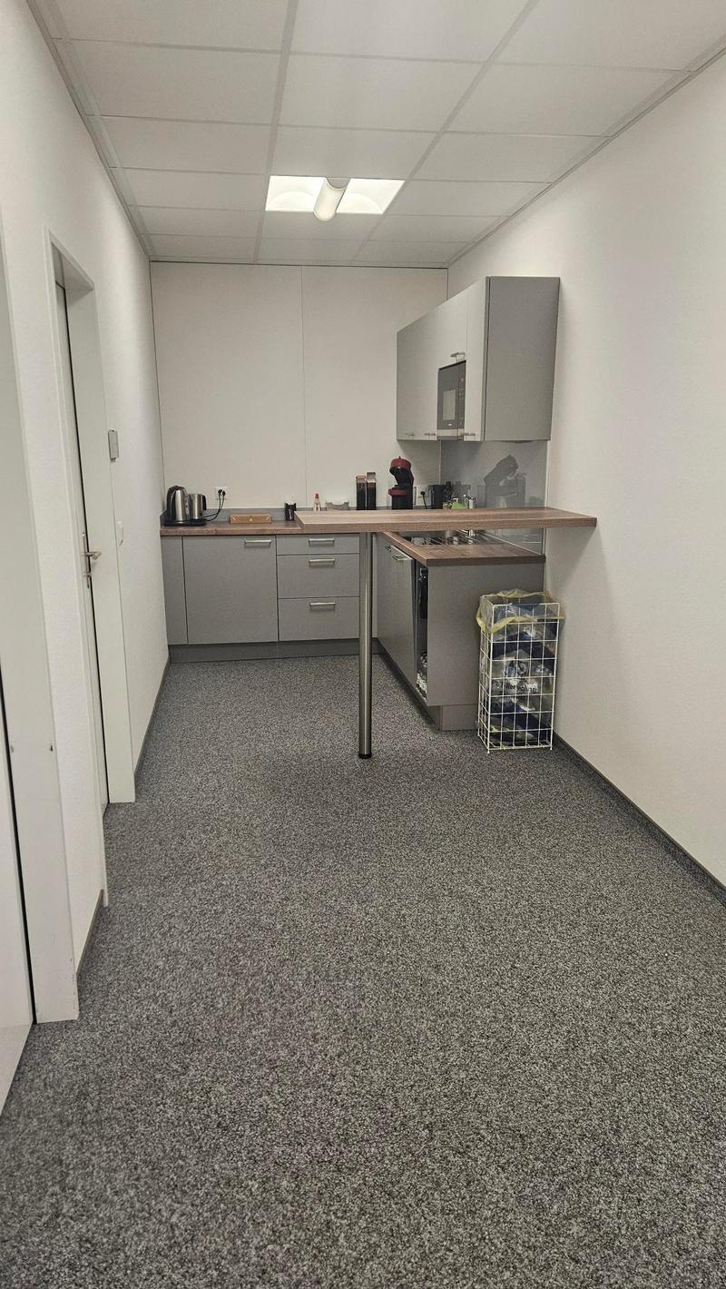 Small office kitchen with gray cabinets, countertop, microwave, and a washing machine and dishwasher. The floor is covered in gray speckled linoleum tiles.