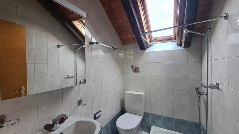 tiled walls, wooden ceiling, white toilet, white sink, blue-tiled bathtub, skylight, silver shower fixtures