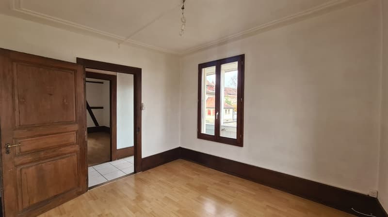 Empty room with wooden door, wooden floor, wooden window frame, white painted walls, and a view from the window