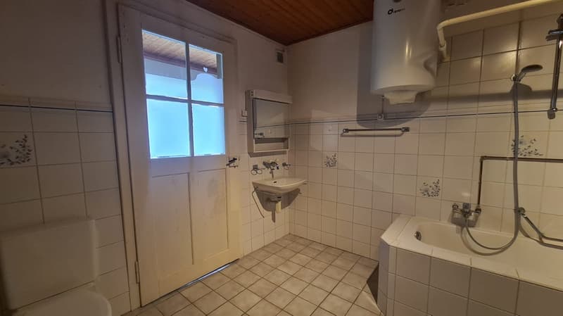 Bathroom with white tiles, bathtub, sink, toilet, shower head, and a washing machine