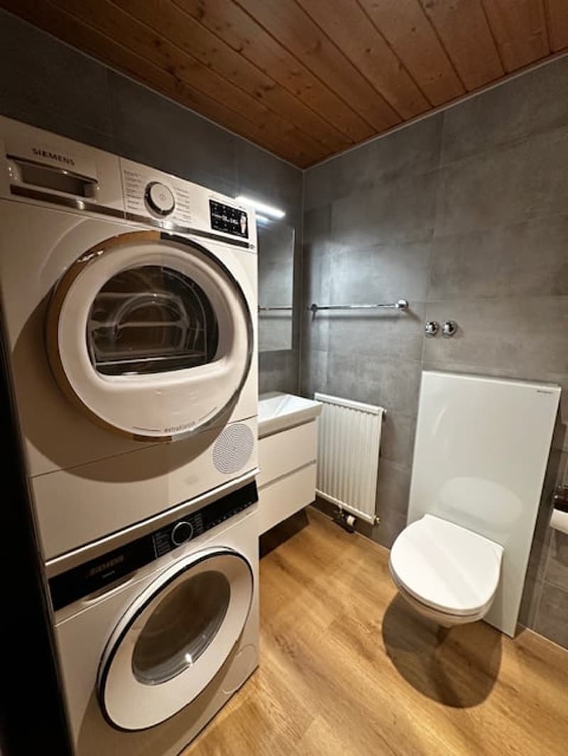 Modern bathroom with a white toilet, wooden floor, a stack of washing machines, and a radiator