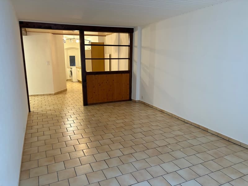 Corridor with tiled floor leading to another room, white walls, wooden door, washing machine in the background