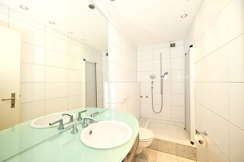 modern bathroom with white tiles, green countertop, double sink, shower, toilet, mirror