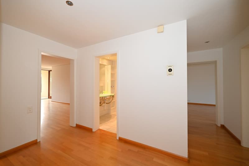 Empty room with white walls, wooden floor, and a door leading to a bathroom.