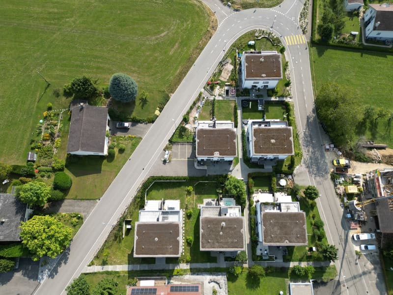 Aerial view of a residential area with several houses, a road, and a green field.