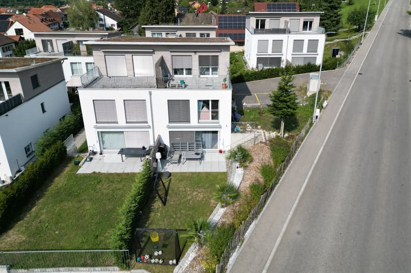 Modern two-story house with solar panels, balconies, and a garden with a terrace.