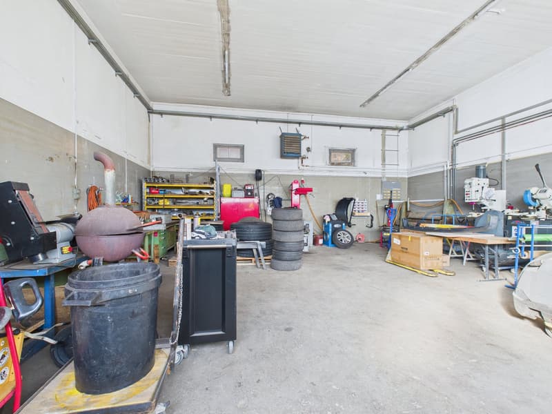 well-lit, spacious, equipped with various tools and machinery, tires stacked in the corner, workbenches, yellow box on a pallet, car jack in the background