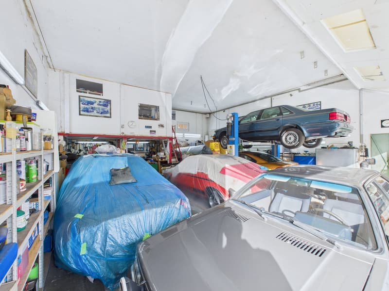 Several cars parked, some under cover, tools and equipment visible, industrial shelving