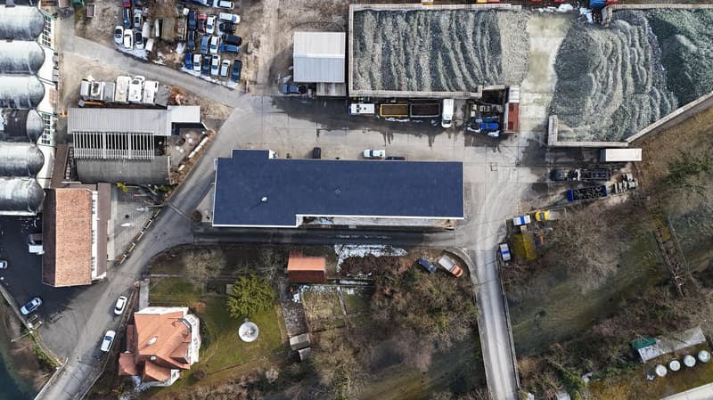 Buildings with parking spots in front of it, several cars parked, gravel storage, road