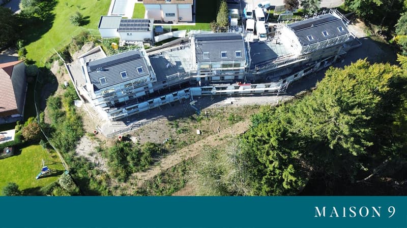 Building with balcony, in construction phase, surrounded by trees and grass, several windows, solar panels