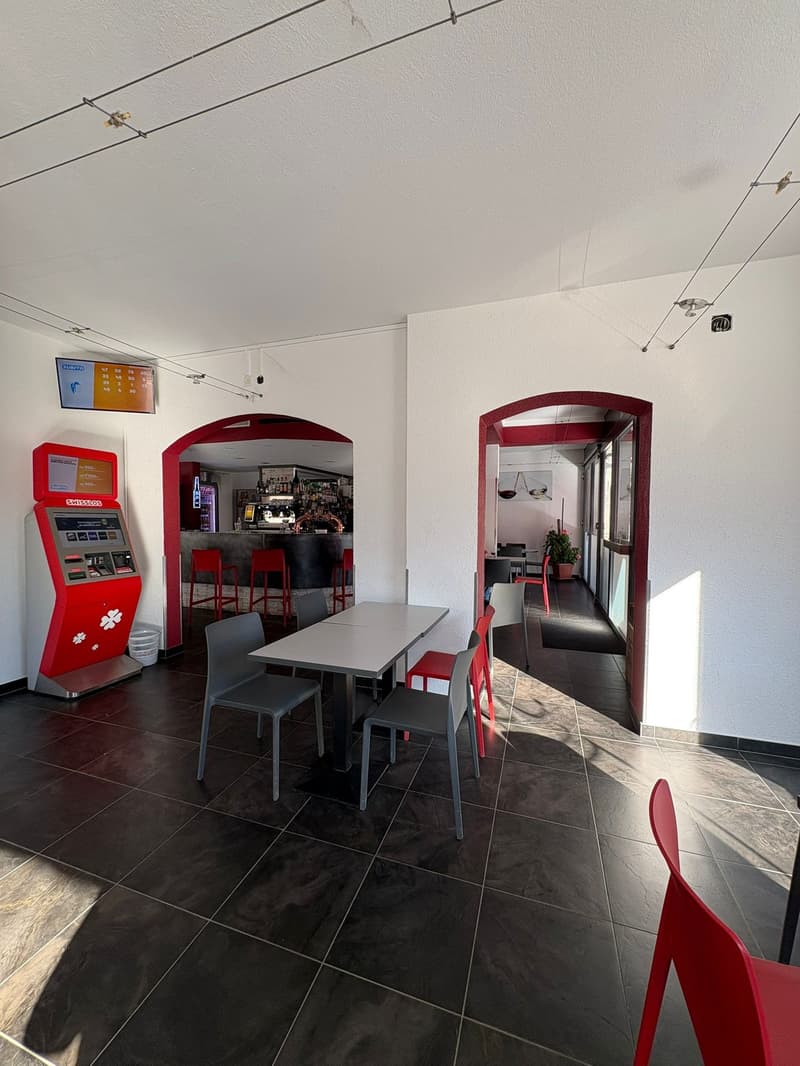 Room with tile floor, ATM machine, chairs and table, counter with barstools, plant, and surveillance camera