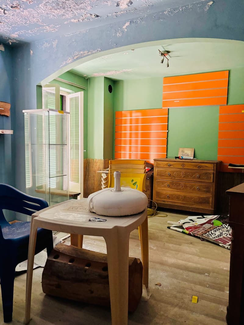 This image shows a room with green walls, orange cabinets, a wooden dresser, and a small table with a decorative item on it. There appears to be a dishwasher visible in the room as well.