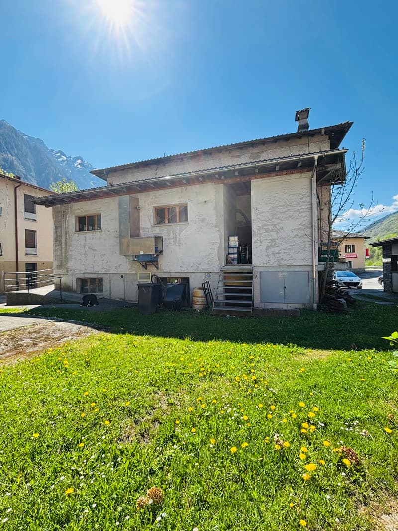 Single-story building with a slanted roof, surrounded by a grassy area with yellow flowers. The building appears to be a residential or commercial property located in a mountainous area with clear blue skies.