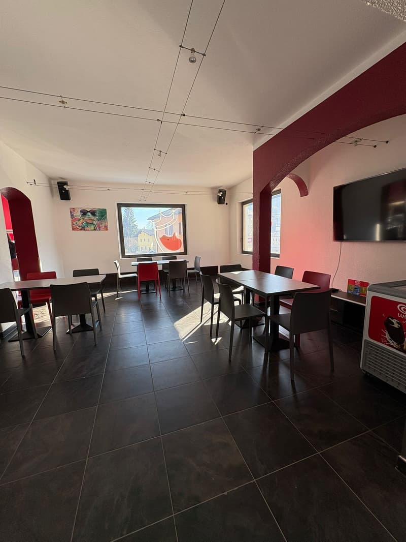 Dining area with tables, chairs, black tiled floor, red walls, speakers, large windows, TV