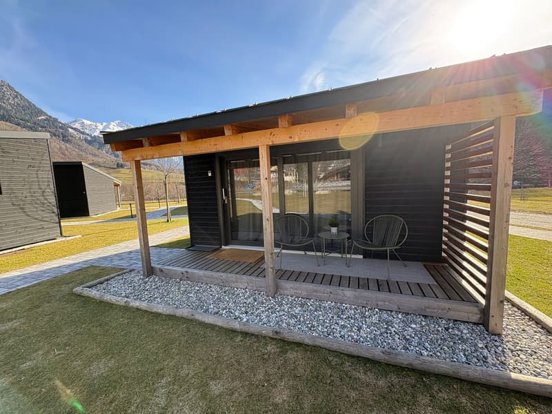 Modern cabin exterior with wooden porch, two chairs, table, glass door and windows