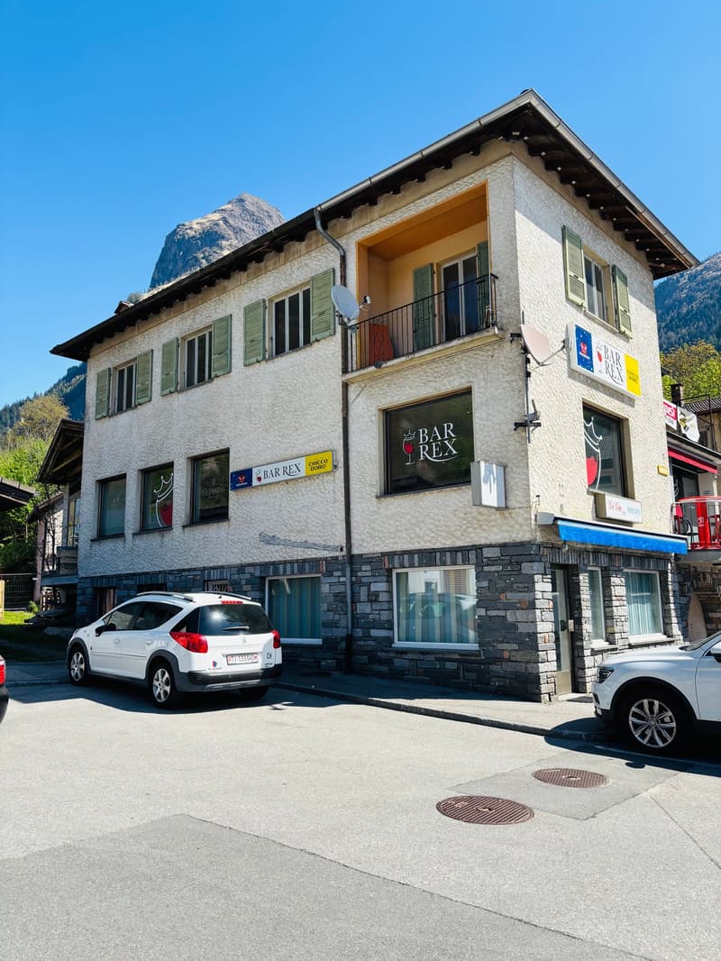 2-story building with stone and stucco exterior, green shutters, balconies, Bar Rex sign, parked cars in front