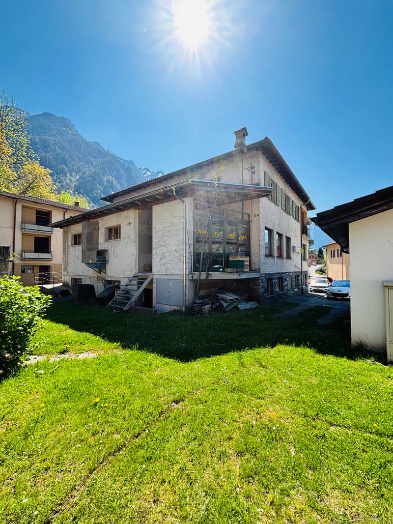 2-story building with a balcony, surrounded by a grassy area and mountains in the background. The building appears to be a commercial or residential property.