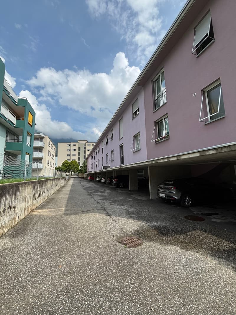 Multi-story apartment building with purple exterior, paved parking area in front, and cars parked along the side of the building
