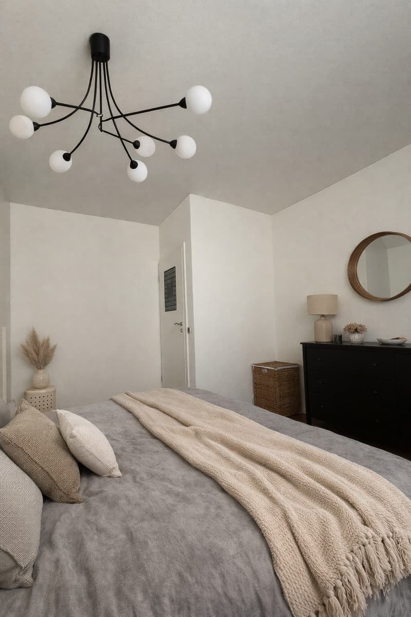 A bedroom with a bed, pillows, a blanket, a lamp, a mirror, a cabinet, and a chandelier