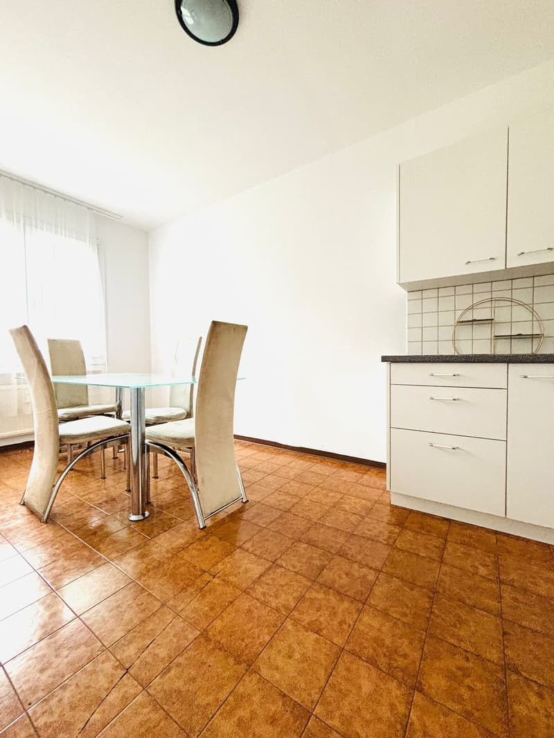 Dining room, glass table, beige chairs, white kitchen cabinetry, tiled floor, white wall, window with white curtains