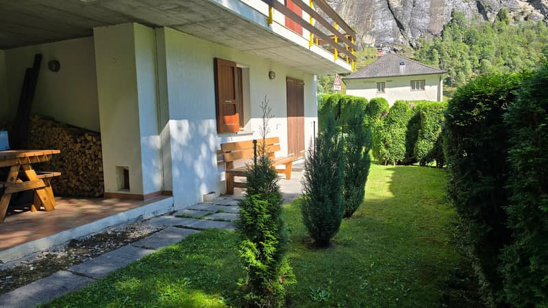 Two story house, white walls, wooden door, wooden bench, wooden table, grass garden, balcony