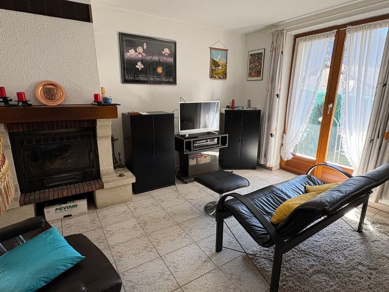 Living room with fireplace, black leather sofa, ottoman, TV, black cabinets, rug, framed pictures, and decorative items