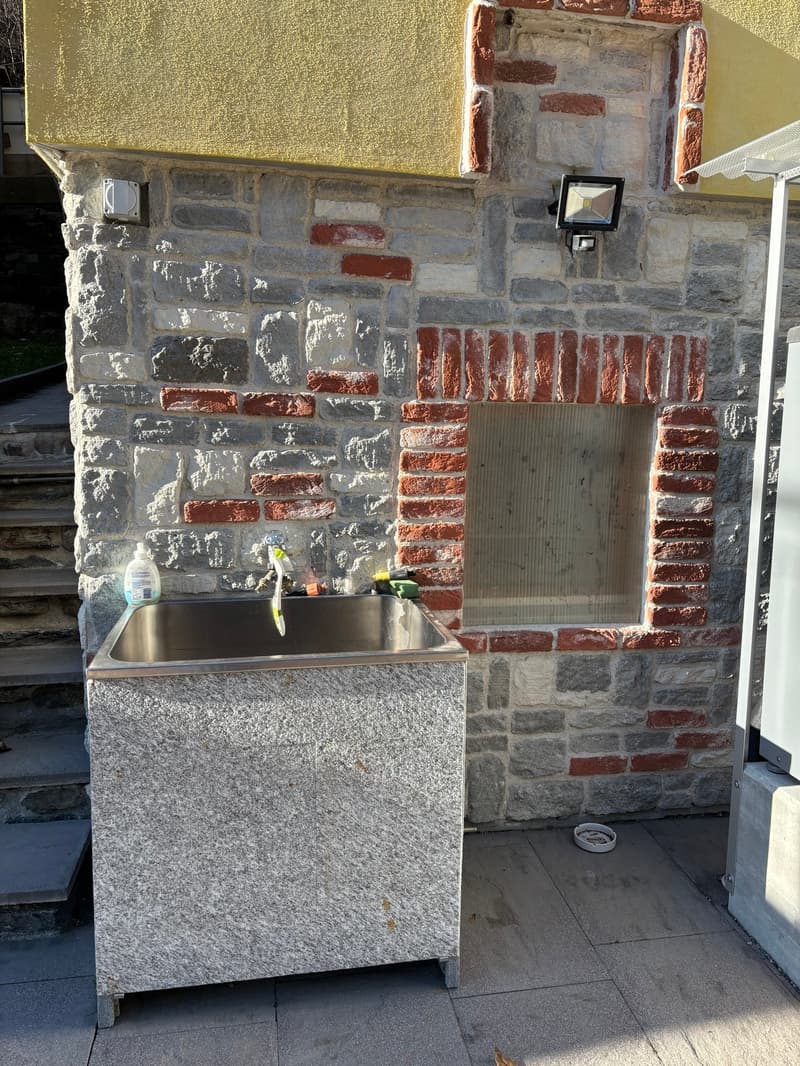 A stone wall, brick pattern, outdoor sink with faucet, small dish next to sink