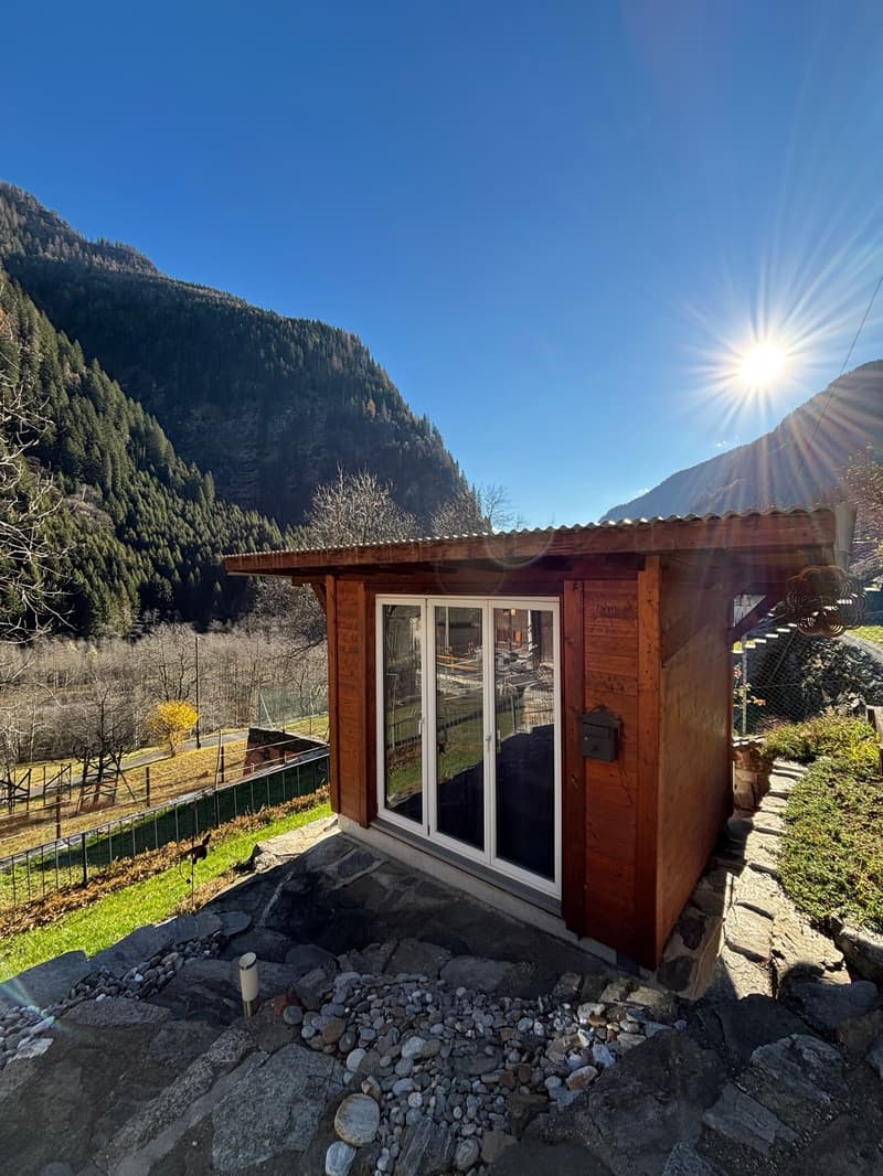 wooden house with glass doors, located in a mountainous area with lush vegetation, surrounded by green areas, stones and grass.