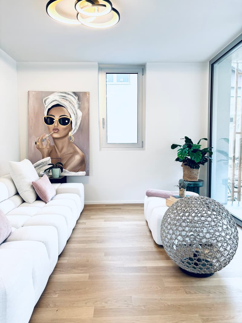 Living room with white couches, wooden floor, round table, and large art painting
