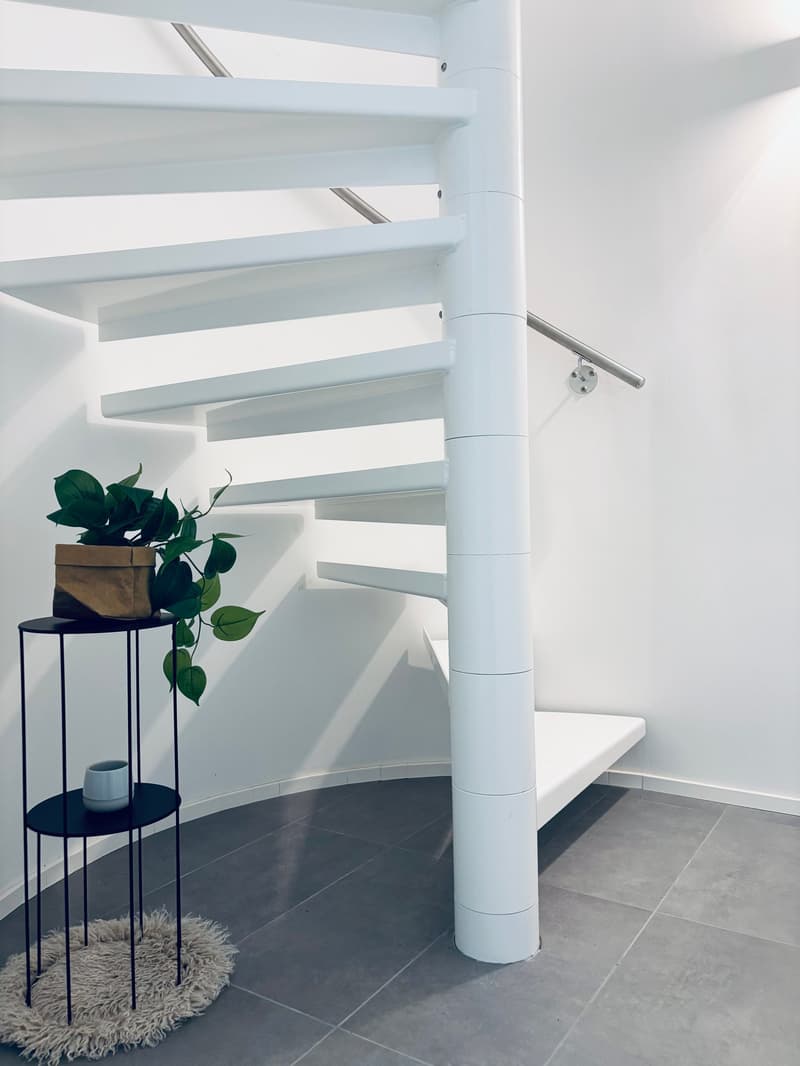 spiral staircase, white tiles, black handrail, grey tile floor, grey wall, plant