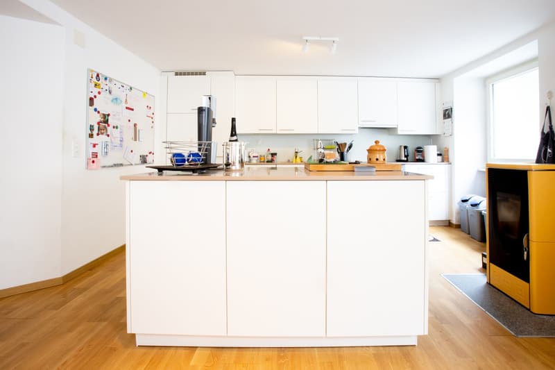 Bright and modern kitchen with white cabinets, wooden countertops, and various kitchen appliances and utensils. There is a dishwasher visible on the counter.